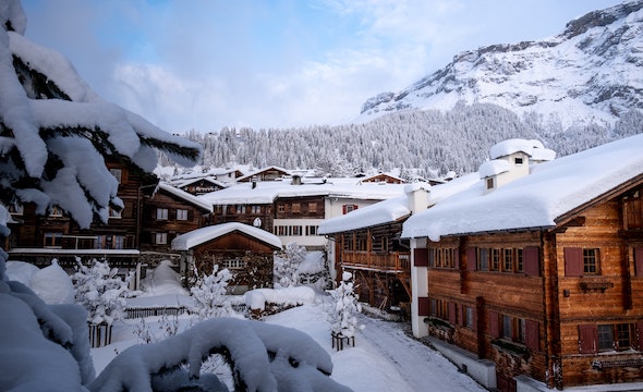 Snow covered wooden cabins with mountains in the background.