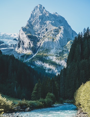 A river with trees on the sides and a snow covered mountain in the background.